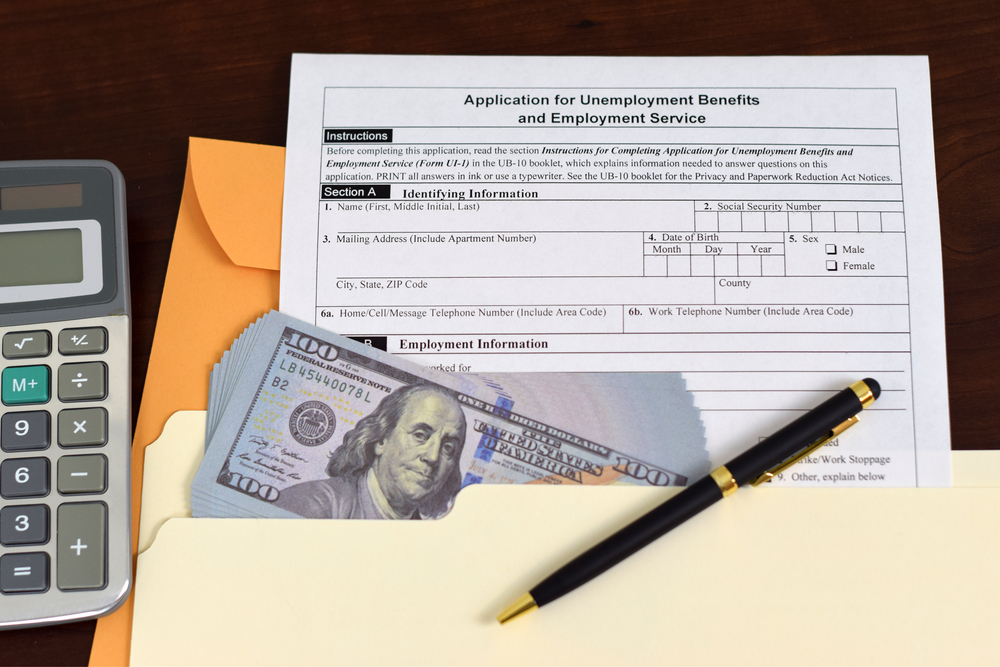 Application for unemployment benefits form with a stack of cash, pen, and calculator.