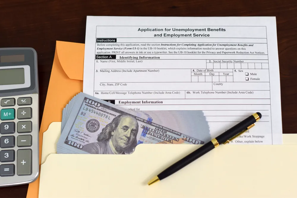 Application for unemployment benefits form with a stack of cash, pen, and calculator.
