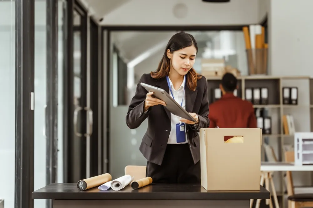 Woman in a suit packing office belongings into a box, preparing to leave her workplace.